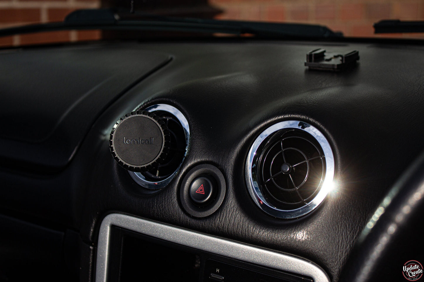 magnetic phone holder inside a mazda mx5. the holder replaced oneof the factory air vents on the dash with a3D printed item that serves to hold your phone while driving.