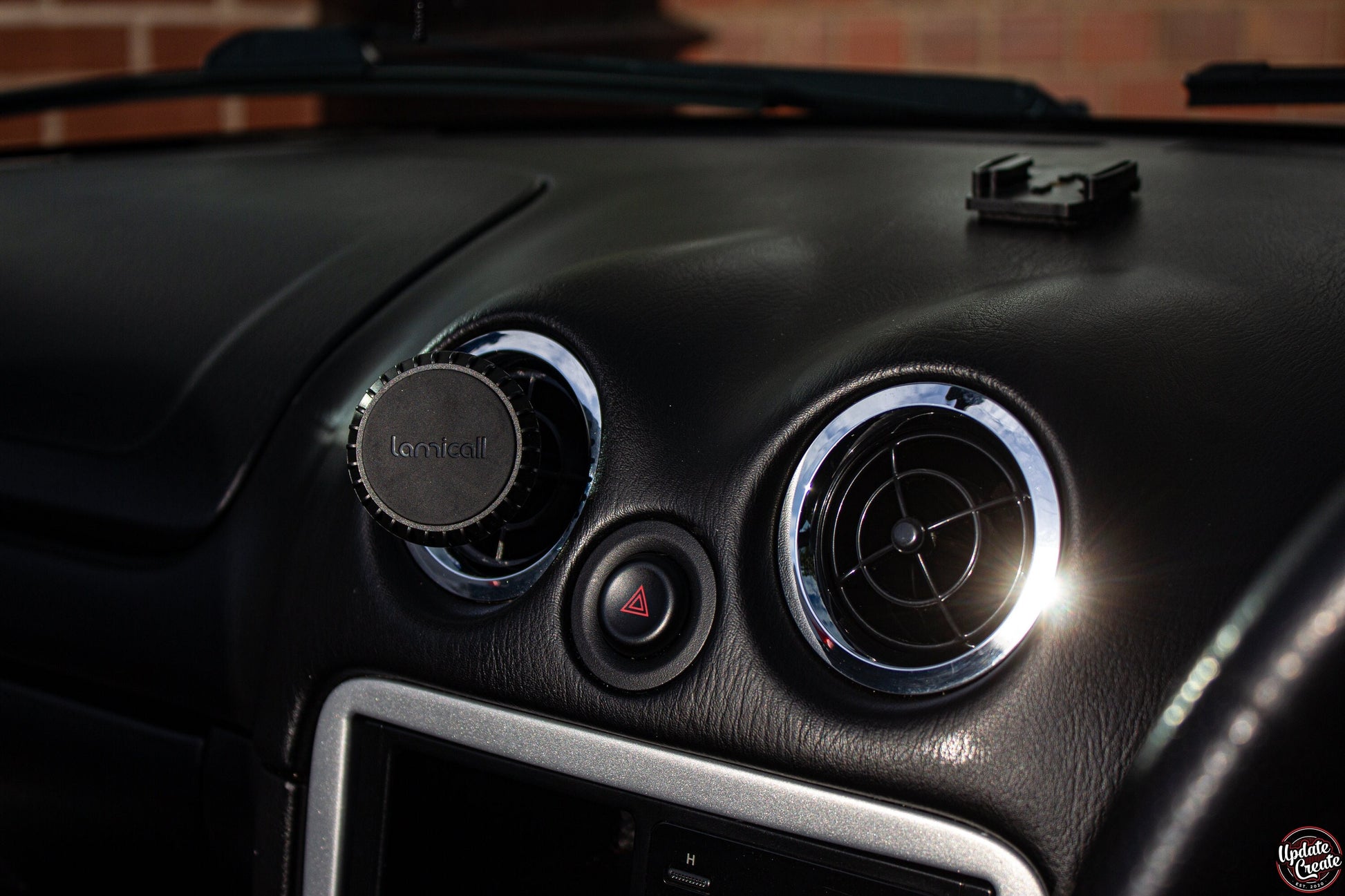 magnetic phone holder inside a mazda mx5. the holder replaced oneof the factory air vents on the dash with a3D printed item that serves to hold your phone while driving.